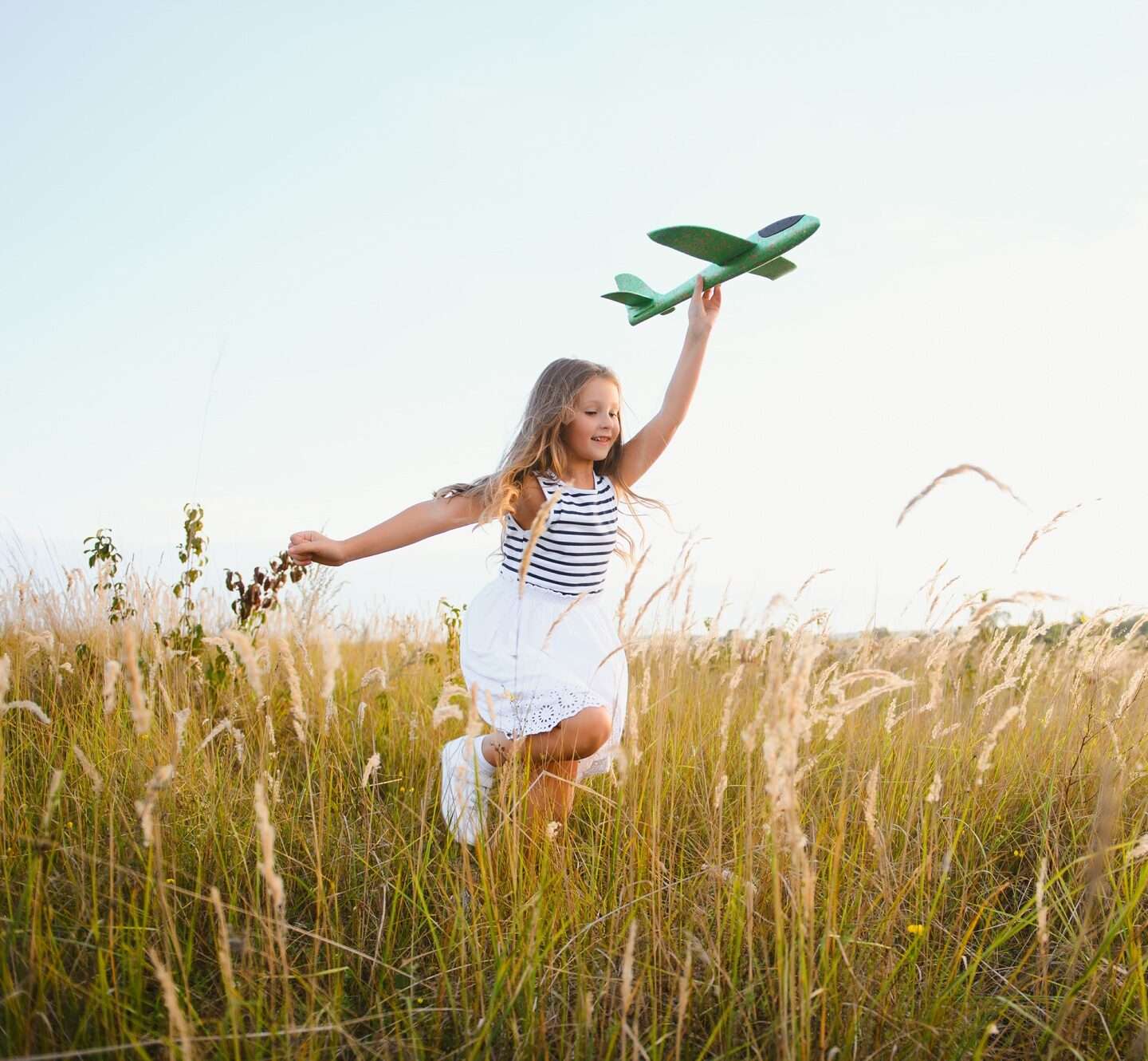 Happy kid with toy plane is playing at sunset