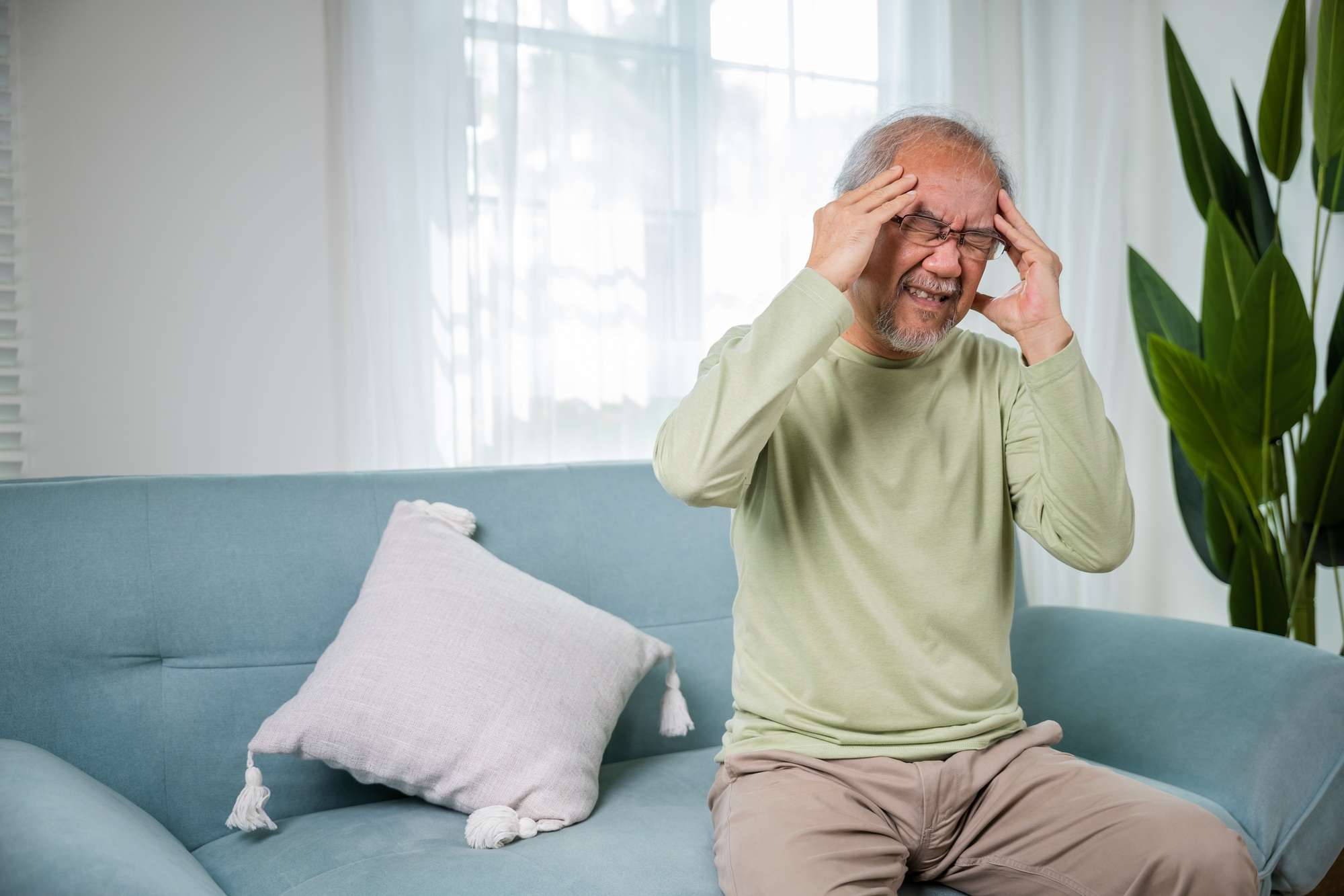 Sad Asian senior man chronic migraine pain massaging