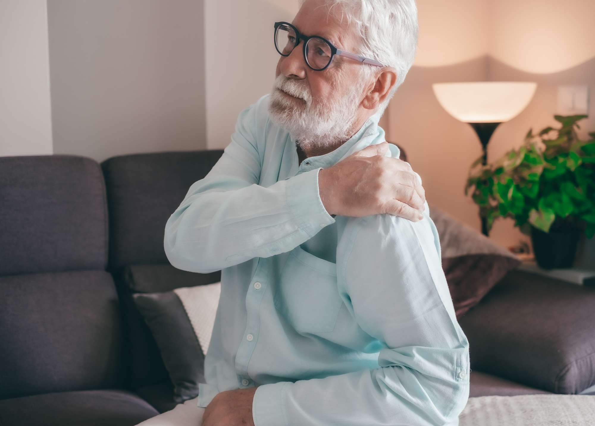 Senior elderly man feels sudden shoulder pain, muscle and neck pain, tension injury at home